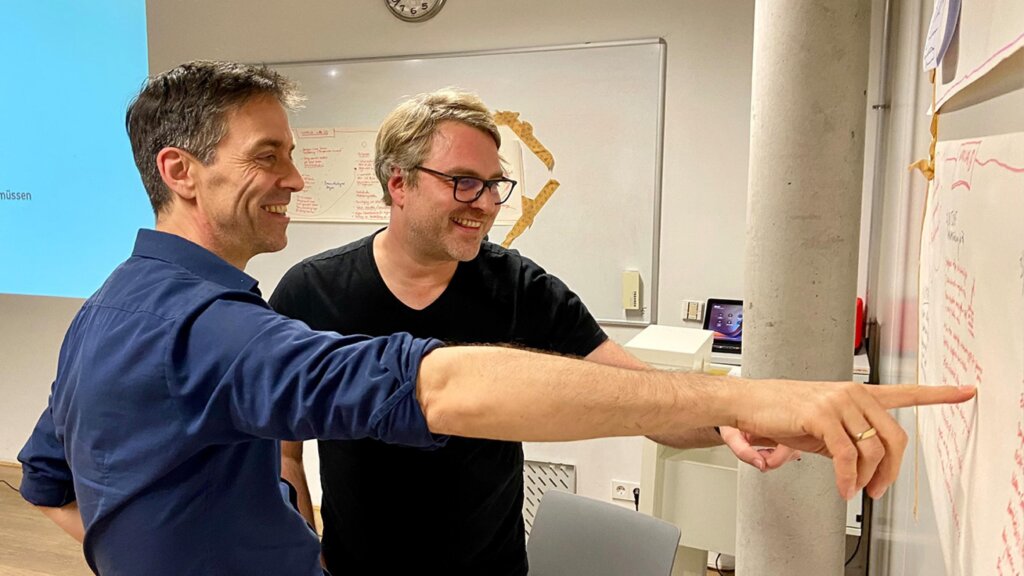Zwei Männer zeigen auf ein Flipchart und bewerten die darauf notierten Ideen